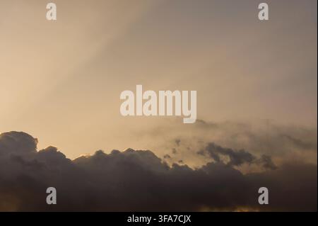 Dramatic dramatic storm clouds illuminated by a bright golden sun beam along the edges during a warm sunset or sunrise sky. Stock Photo