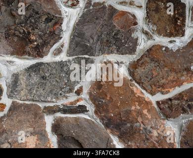 Horizontal close up of a multi color rock wall with varied stones in wide porous cracked mortar joints, showing rough textures Stock Photo
