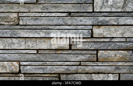 Horizontal close up of sawn unpolished granite blocks set in recessed mortar, showing mixed gray and white stone with brown and gold mineral veining Stock Photo