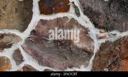 Close up of a multicolor rock wall surface with porous, uneven stones surrounded by wide cracked mortar joints filling the gaps between them Stock Photo