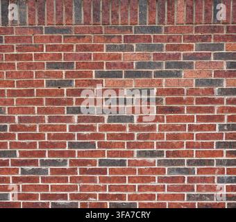 Close up of a red brick wall surface with scattered black bricks, variegated bricks and porous even mortar with a vertical top row of bricks Stock Photo