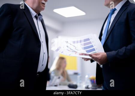 Two businessmen discussing charts and graphs during a professional meeting in an office setting Stock Photo