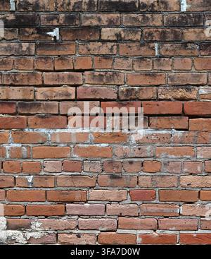 Vertical close-up view of a deteriorating red brick wall surface with cracked broken bricks, some with black smudges Stock Photo