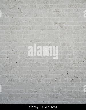 Vertical close-up view of a white painted textured brick wall surface with rough chipped bricks with grooved faces Stock Photo