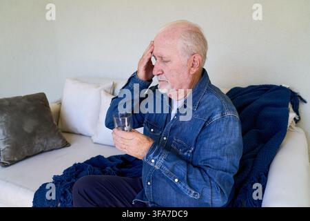 Elderly care and home healthcare, senior man with a headache taking self medication with a glass of water. Patient suffering from pain and illness, re Stock Photo