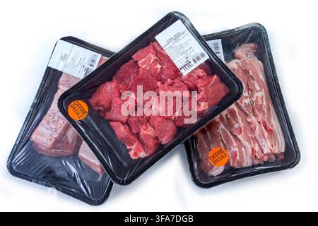 Three black plastic trays containing raw meat are wrapped in clear plastic on a white background. Two trays feature orange circular stickers. Raw meat Bsip 016952 153 Stock Photo