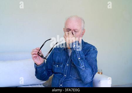 Elderly care and home healthcare, senior man experiencing headache and eye strain, self medication and wellness concept. Mature male patient holding g Stock Photo