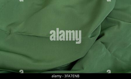 A close up view of a smooth green fabric surface showing gentle undulating folds and a seamless texture, The dark olive colored material drapes natura Stock Photo