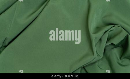 A detailed macro shot of a dark green cloth background featuring dynamic diagonal creases and deep shadows, The richly colored textile flows naturally Stock Photo