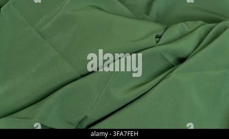 A textured green fabric background displaying prominent folds and tight creases intersecting across the view, The deep forest hue highlights the dense Stock Photo