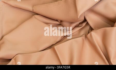 A detailed view of a folded beige cloth highlighting a raw edge with delicate fraying threads along the upper section, The smooth tan fabric cascades Stock Photo