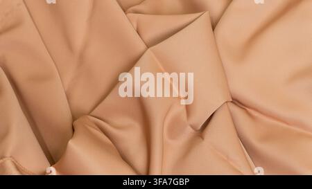 A sophisticated beige fabric background characterized by sharp angular folds and deep intersecting creases, The smooth tan material displays a structu Stock Photo