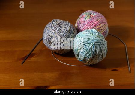 A studio photograph featuring three balls of multicolored speckled yarn (grey, pink, and light green) accompanied by circular knitting needles, arrang Stock Photo