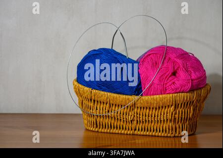 A close-up horizontal photograph showing a woven straw basket resting on a polished wooden surface against a neutral grey wall. Inside, vivid magenta- Stock Photo