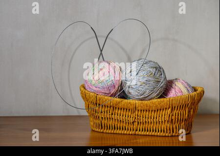 A studio photograph featuring a wicker basket filled with several balls of multicolored speckled yarn, with circular knitting needles inserted into th Stock Photo