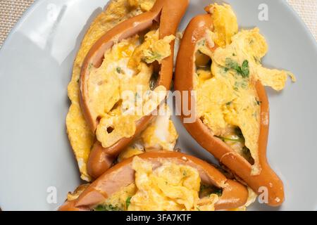Split sausages are packed with golden scrambled egg and chopped parsley arranged on a plain white plate. The top down composition highlights the gloss Stock Photo