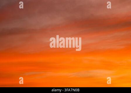 Stunning sunset or sunrise sky filled with dramatic fiery orange and red clouds, creating a colorful natural background texture. Stock Photo