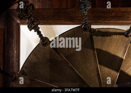 A close view of a historic wooden spiral staircase shows ribbed steps and an ornate central column with decorative detailing. Stock Photo