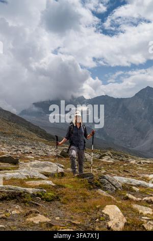 A hiker explores the rocky alpine landscape of Almagellertal in the Swiss Alps under a dynamic sky. The scene captures adventure and the beauty of unt Stock Photo