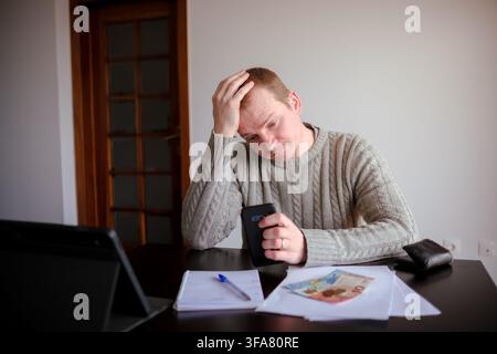 Man holding smartphone, calculating bills and feeling stressed about financial debt Stock Photo