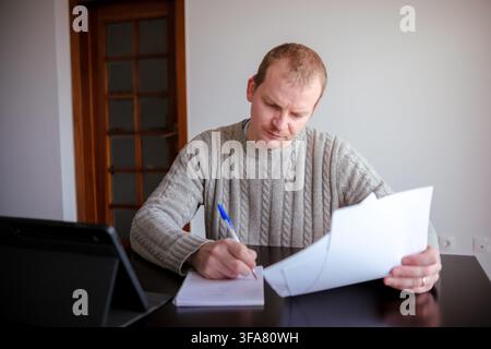 Man focusing on paperwork, writing on a notebook, and holding documents at a desk Stock Photo