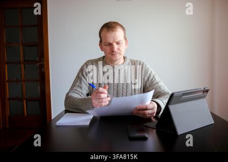 Man working from home, reviewing paperwork and information on a tablet Stock Photo