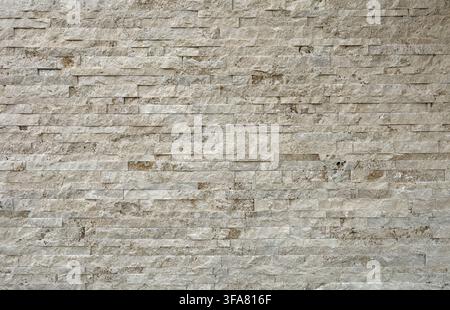 Stone coating wall made of striped stacked slabs of off-white travertine bricks. Background and texture. Stock Photo