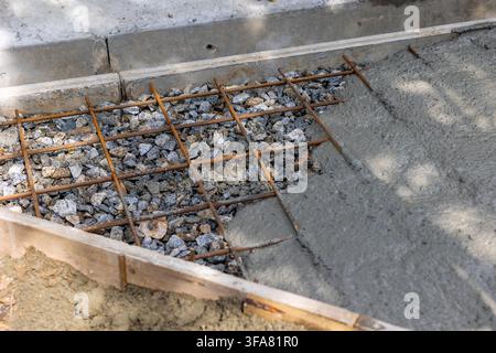 Wet cement filling rebar wire mesh over crushed stone layer in backyard daylight. Concept: concrete pouring process Stock Photo