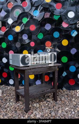 Grey retro radio player with speakers on dark high stool is placed on small round stones surface during outdoor exhibition near decorative gramophone Stock Photo