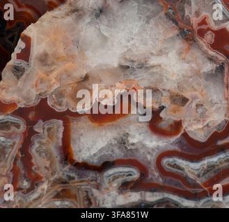Close-up macro texture of a polished banded agate stone featuring intricate red, white, and translucent quartz crystal layers. Stock Photo