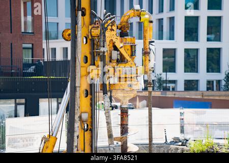 Yellow hydraulic rotary drilling rig mast with kelly bar drive head and auger drill bit operating on urban foundation construction site Stock Photo