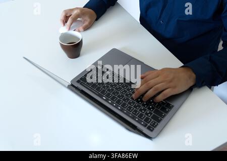 High angle close-up of a businessman in a dark blue shirt typing on a laptop keyboard, using a white computer mouse Stock Photo