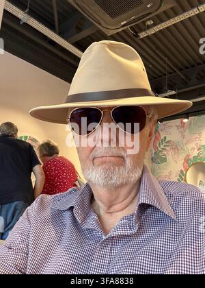 A stern faced man wearing sunglasses and a pamana style hat indoors. Stock Photo