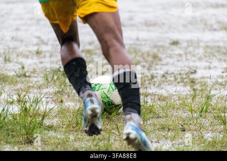 Boy kicking soccer ball in rainy season Stock Photo