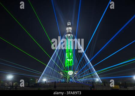 View of the Minar-e-Pakistan monument illuminated with vibrant green and blue laser light beams against the night sky in Lahore, Punjab, Pakistan. Stock Photo