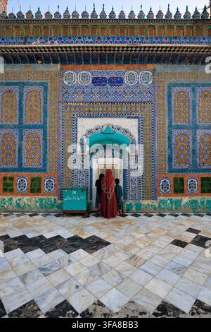 View of the intricate tile work at the entrance of Darbar Hazrat Sultan Bahoo, with a woman in a red veil and children standing on the marble floor in Stock Photo