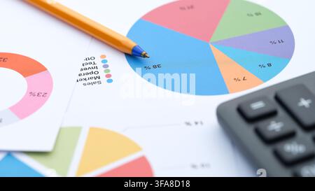 A close-up shot of financial documents featuring colorful pie charts, a yellow ballpoint pen, and a calculator. Stock Photo