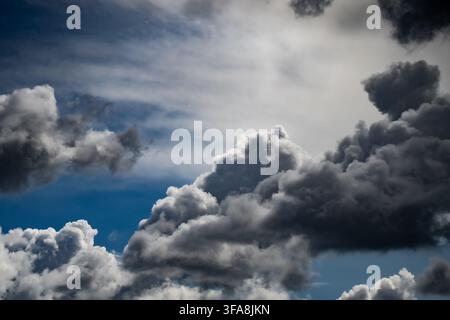 Dramatic stormy sky with heavy dark rainclouds contrast against bright blue sky during meteorology weather change Stock Photo