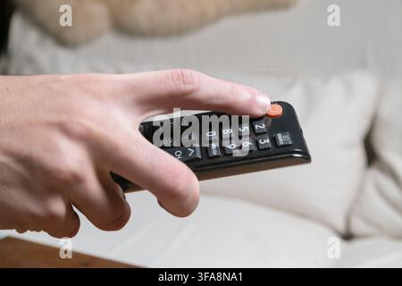 Hand pressing red power button on TV remote control, close up cropped view at home Stock Photo