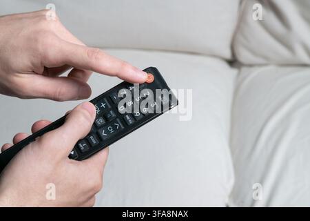Person's hand pressing power button on a universal remote controller for television Stock Photo
