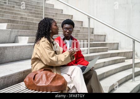 African american friends man woman students talking sharing ideas while working outside on laptop. Stock Photo
