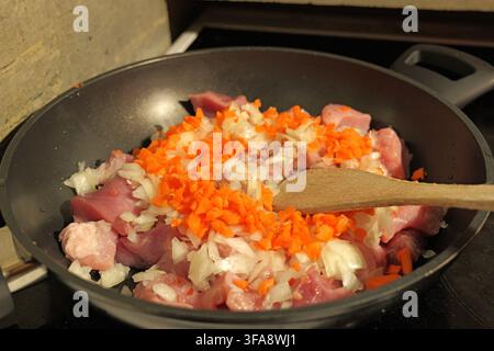Raw pork pieces, fresh diced carrots, and chopped onions combine in a black frying pan, ready for stir frying or simmering to prepare a delicious home Stock Photo