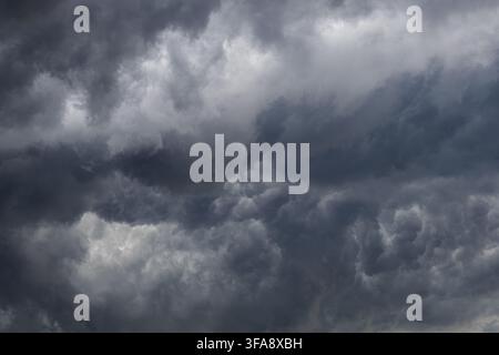 Massive dark storm clouds forming a dramatic and turbulent cloudscape before severe weather. Dense layered clouds with contrasting light create an omi Stock Photo