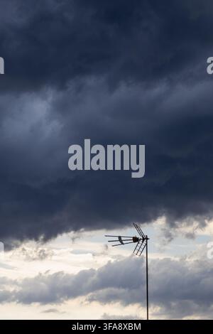 A television antenna silhouetted against massive dark storm clouds and a bright opening in the sky. The dramatic cloud formation creates a powerful se Stock Photo