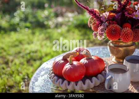 Fall table decor in autumnal garden. Close up of bouquet of dahlia flowers, orange pumpkins and coffee for two in backyard. Space Stock Photo