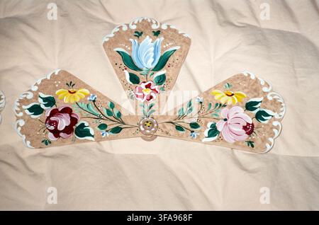 A beautifully hand-painted decorative fan with colorful folk art floral motifs including roses, tulips, and daisies on a tan background, displayed on Stock Photo