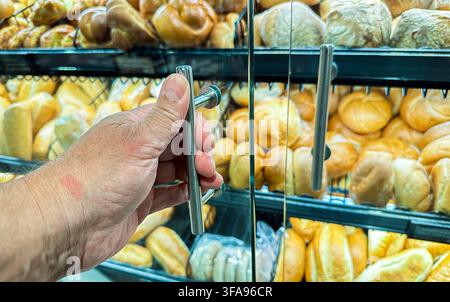 Customer's hand reaching for fresh bread and rolls in a bakery display case Stock Photo