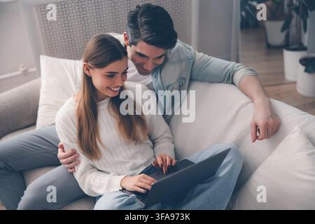 Happy young couple using a laptop together while relaxing on a sofa in a bright modern living room at home Stock Photo