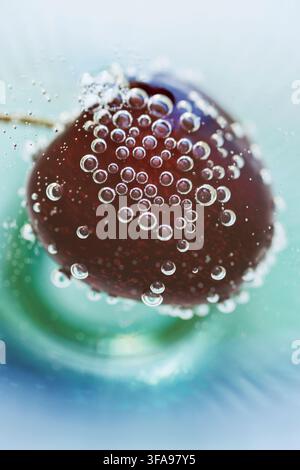 Close up macro of a ripe cherry surrounded by tiny sparkling bubbles in clear mineral water highlighting freshness, natural beauty, healthy nutrition Stock Photo