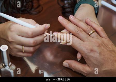 Manicurist painting fingernails with light pink polish at a nail salon Stock Photo